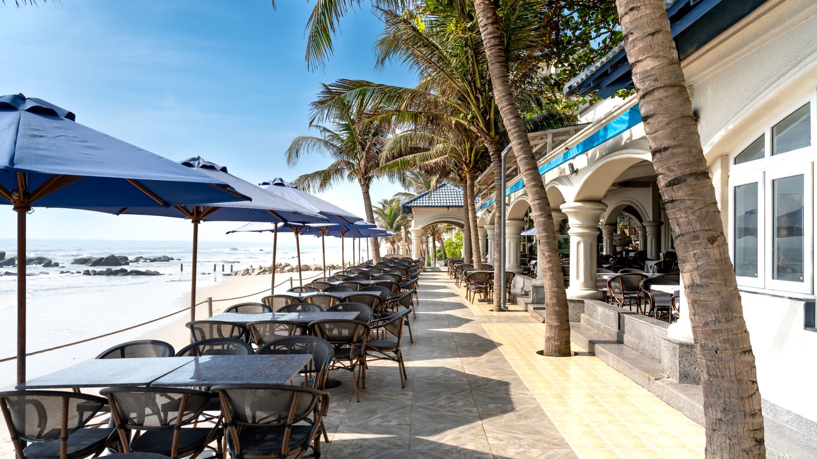 Beachfront restaurant tables under blue umbrellas